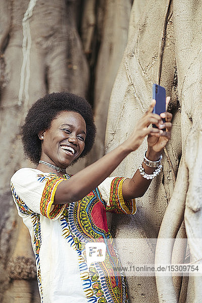 Lachende junge Frau  die mit einem Smartphone einen Selfie macht