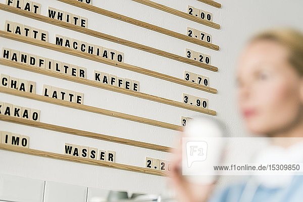 Price board in a coffee shop with customer carrying cup of coffee