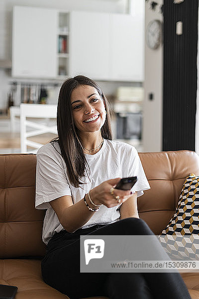 Happy young woman sitting on couch at home watching Tv