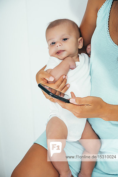 Mother using smartphone and holding her baby