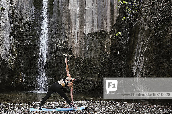 Frau praktiziert Yoga am Wasserfall  Dreieckshaltung