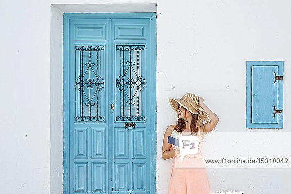 Redheaded young woman with book standing in front of a house looking at distance Frigiliana Malaga Spain