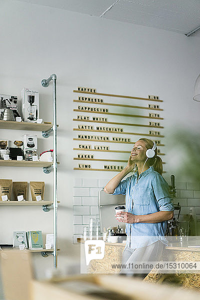 Young woman listening music  wearing headphones  standing in coffee shop