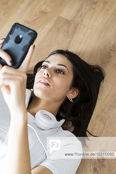 Junge Frau mit Smartphone auf dem Boden liegend