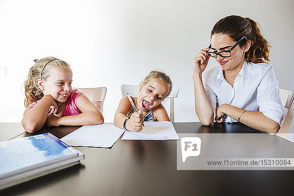Lehrer sitzt am Schreibtisch mit zwei glücklichen Schulmädchen  die auf Papier schreiben