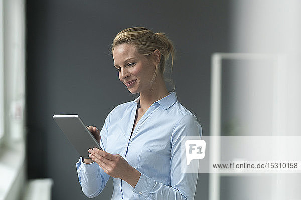 Lächelnde junge Geschäftsfrau benutzt Tablette im Büro