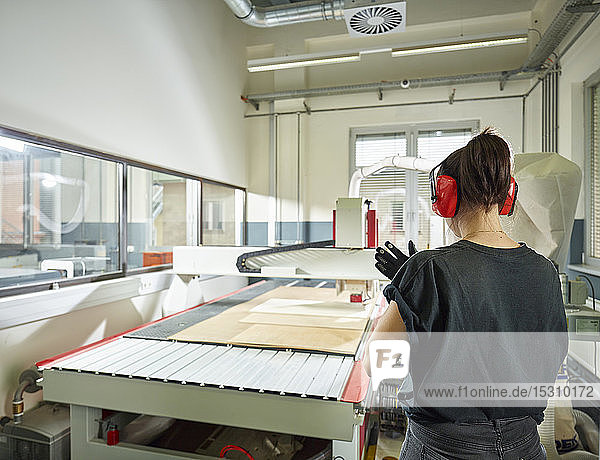 Rückansicht einer Frau an einer CNC-Maschine in der Werkstatt