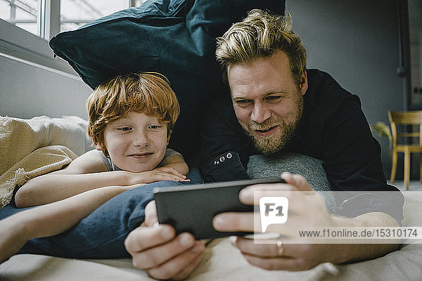 Porträt von Vater und Sohn  die auf der Couch liegen und auf ein Handy schauen