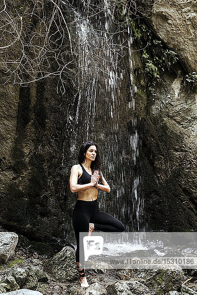 Frau praktiziert Yoga am Wasserfall  Baumposition