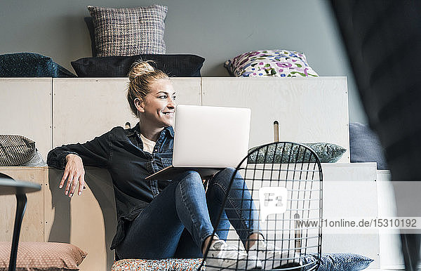 Smiling casual businesswoman using laptop in office lounge