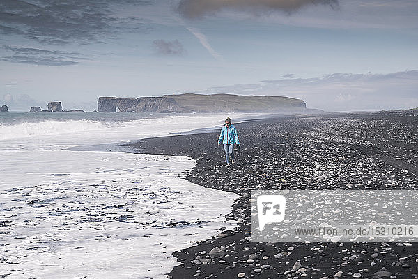 Junge Frau geht barfuss an einem Lavastrand in Island