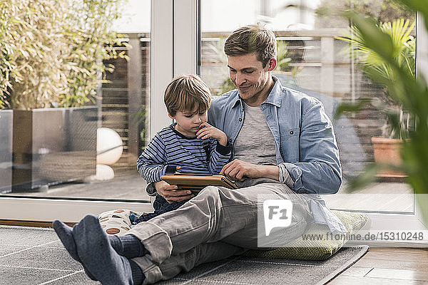 Father and son sitting on floor  using digital tablet