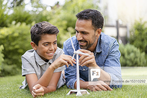 Lächelnder Vater und Sohn liegen mit einem Modell einer Windkraftanlage im Garten