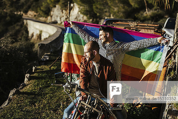 Schwules Paar mit schwuler Stolz-Fahne auf einem Motorrad