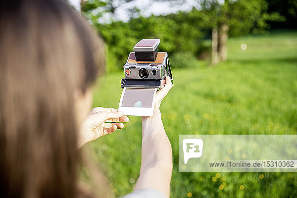 Nahaufnahme einer Frau die ein Sofortfoto auf einer Wiese macht