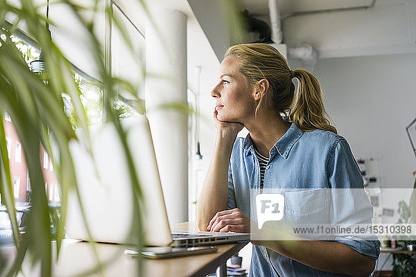 Blonde Frau sitzt im Café  benutzt einen Laptop und schaut aus dem Fenster