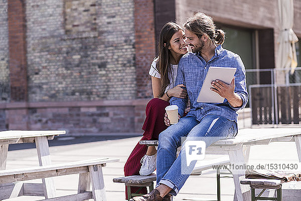 Glückliches junges Paar sitzt mit Tablette am Tisch in einem Biergarten