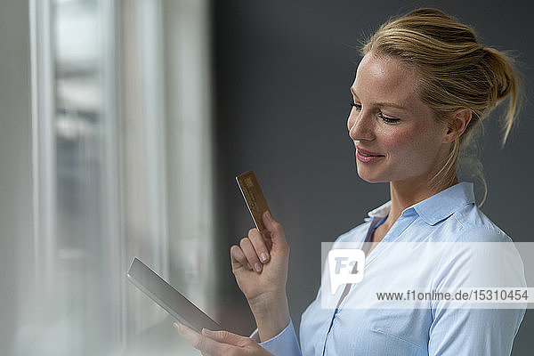 Lächelnde junge Frau mit Tablette und Kreditkarte