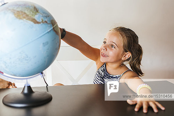 Happy schoolgirl looking at globe on desk