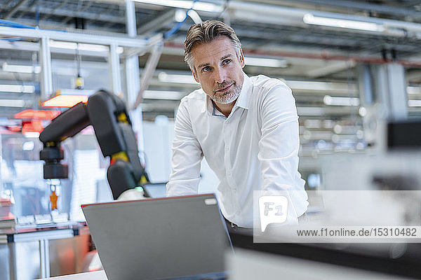 Businessman with laptop in a modern factory hall