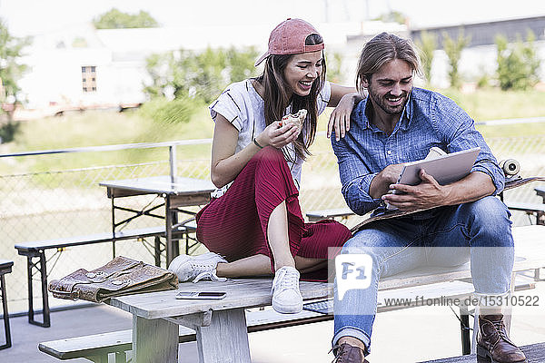 Junges Paar sitzt mit Tablette am Tisch in einem Biergarten