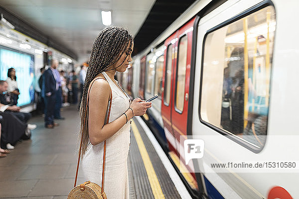 Young woman waiting at subway station platform looking at cell phone  London  UK