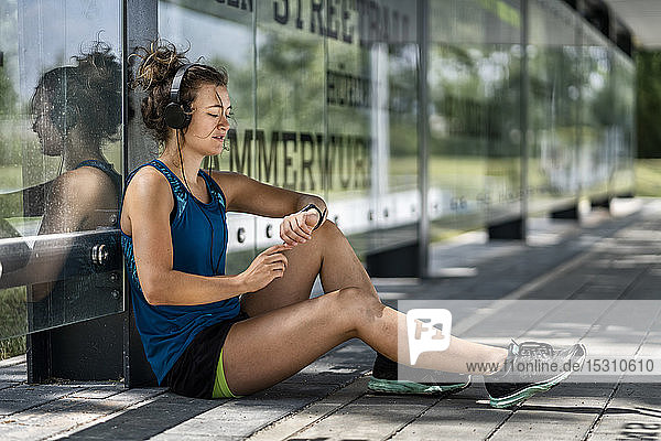 Junge sportliche Frau  die Kopfhörer trägt und ihre Smartwatch kontrolliert