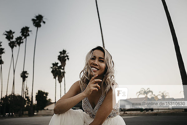 Porträt einer lächelnden Braut  die an einer Straße mit Palmen sitzt