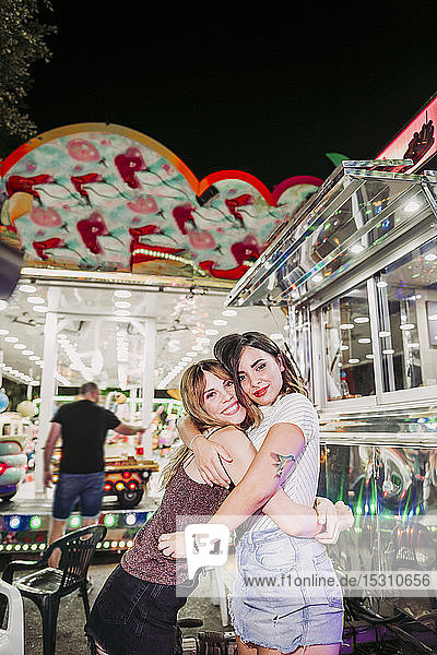 Portrait of two happy young women hugging on a funfair at night