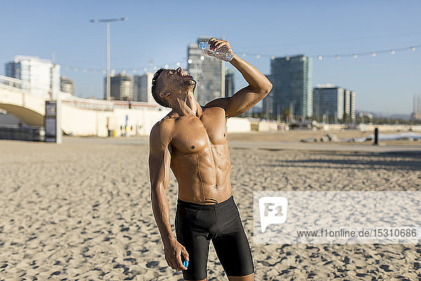 Bleichgesichtiger Mann trinkt Wasser nach dem Training am Strand
