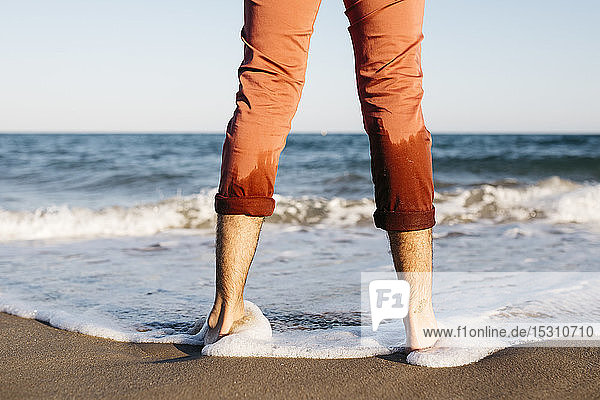Rückansicht eines Mannes mit orangefarbener Hose  der an einem Strand am Wasser steht
