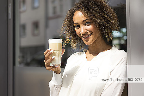 Porträt einer lächelnden jungen Frau  die sich im Straßencafé mit Latte Macchiato entspannt