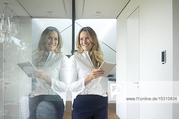 Smiling businesswoman holding tablet in modern home