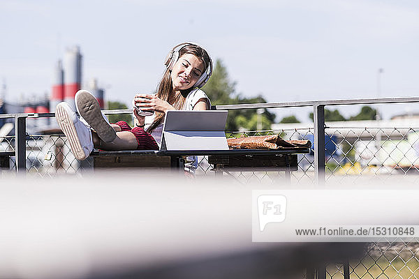 Junge Frau entspannt sich in einem Biergarten mit Kopfhörer und Tablette
