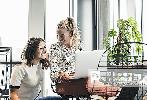 Two happy casual businesswomen with laptop meeting in office