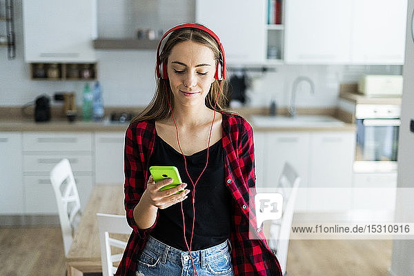 Junge Frau mit Handy und Kopfhörern zu Hause