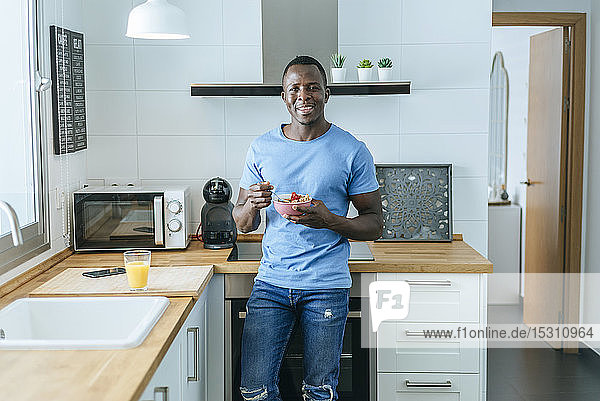 Portrait of young man having breakfast in kitchen at home