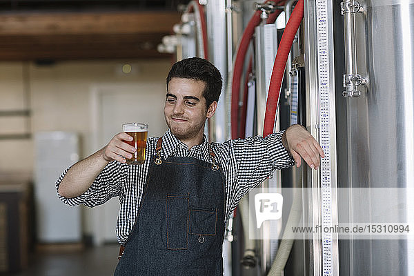 Porträt eines selbstbewussten jungen Mannes mit Bierglas in der Hand in einer Brauerei
