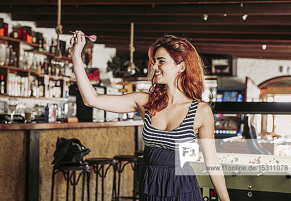 Happy young woman playing darts in a sports bar