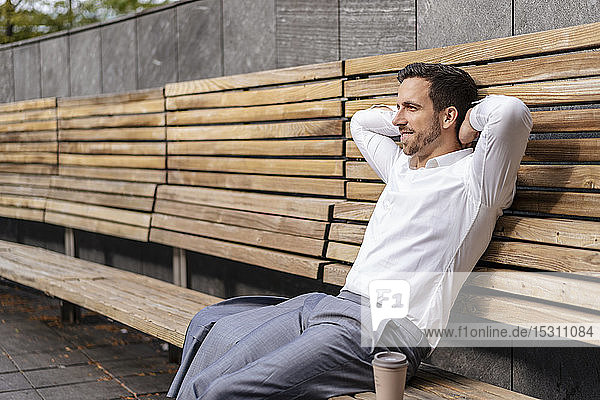 Entspannter Geschäftsmann sitzt auf Holzbank in der Stadt