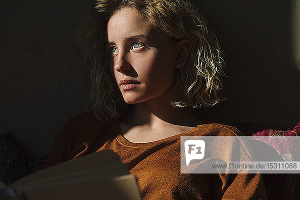 Porträt eines nachdenklichen Studenten mit Buch  der aus der Ferne schaut
