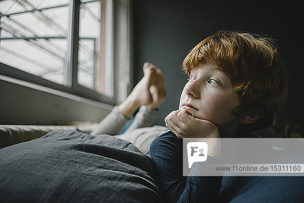Porträt eines rothaarigen Jungen  der auf einer Couch aus dem Fenster liegt