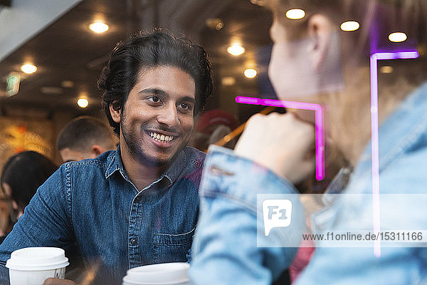 Porträt eines lächelnden jungen Mannes in einem Café  der eine junge Frau ansieht