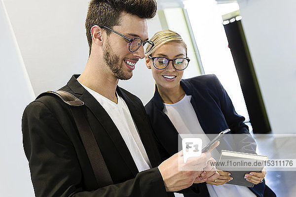 Two smiling young business partners using a smartphone