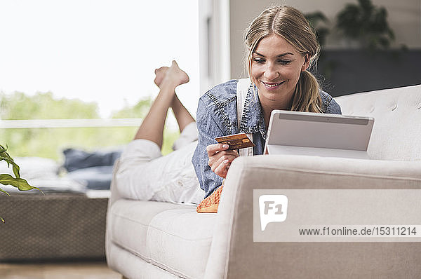 Lächelnde Frau auf Couch mit Kreditkarte und Tablette