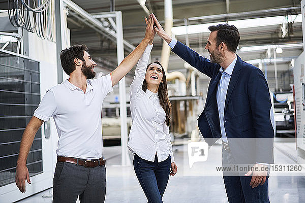 Happy businessman and employees high fiving in a factory