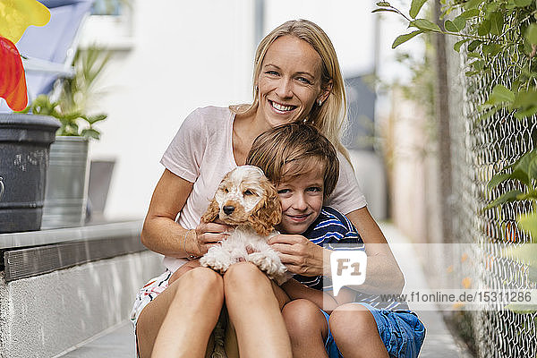 Portrait of mother snd son cuddling with cute dog puppy