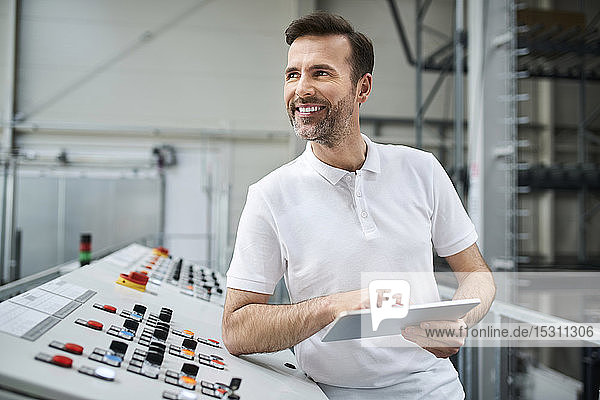 Lächelnder Mann mit Tablette am Bedienpult in einer Fabrik