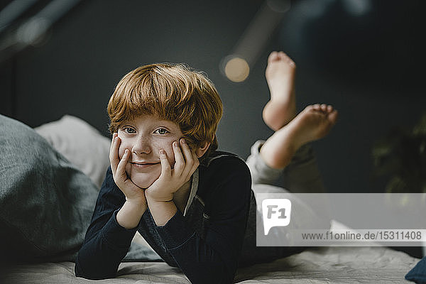 Porträt eines lächelnden rothaarigen Jungen  der zu Hause auf der Couch liegt