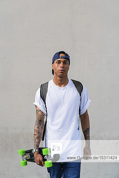 Portrait of tattooed young man with skateboard in front of grey background